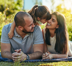 Happy couple lying on the grass with their young daughter, confident their future is secure with Guardian Insurance.