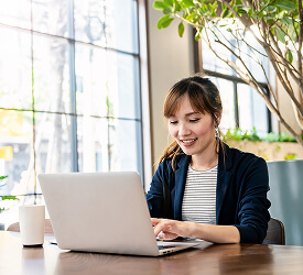 Smiling woman using a laptop in a bright room, representing easy online access to Guardian’s account finder