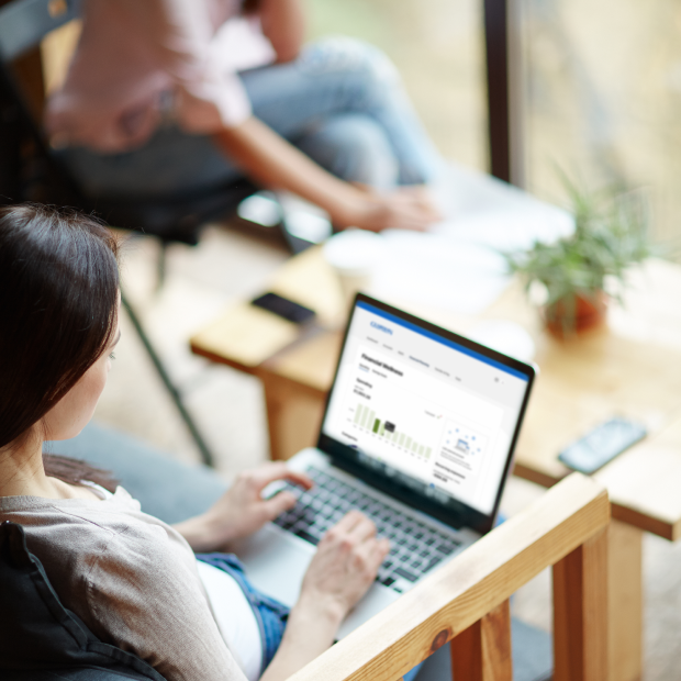 A woman is using a laptop with the Guardian Credit Union online banking dashboard open, seated in a modern workspace with another person nearby and a smartphone on the table.