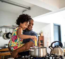Parent holding child while cooking, representing Guardian Credit Union’s support for family life through flexible loan options