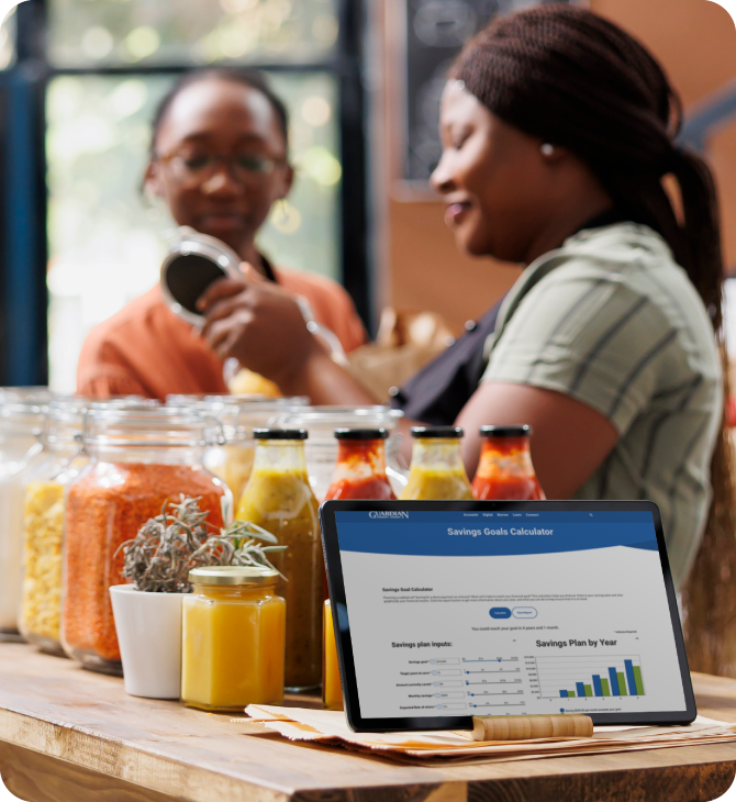 Small business owner in shop uses Guardian CU savings calculator to plan goals and manage inventory
