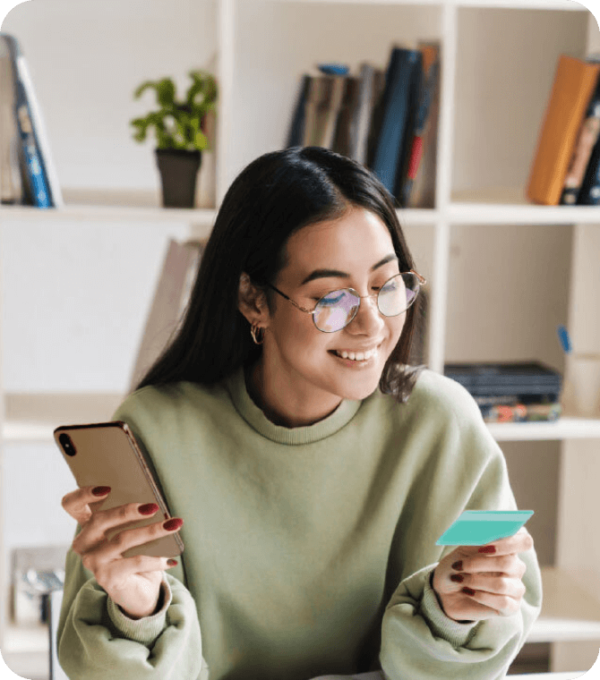 Teen holding smartphone and Greenlight debit card, managing money through Guardian CU youth checking tools