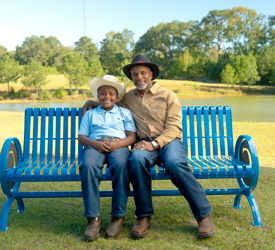 Grandfather and grandson smiling while sitting on a Guardian Credit Union bench at their farm.