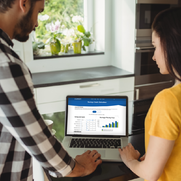 Couple using a laptop in a kitchen to review a Guardian Credit Union's Savings Goals calculator with charts and projections, planning their finances together.