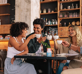 Friends laughing and toasting coffee at a café, representing everyday moments supported by Guardian checking