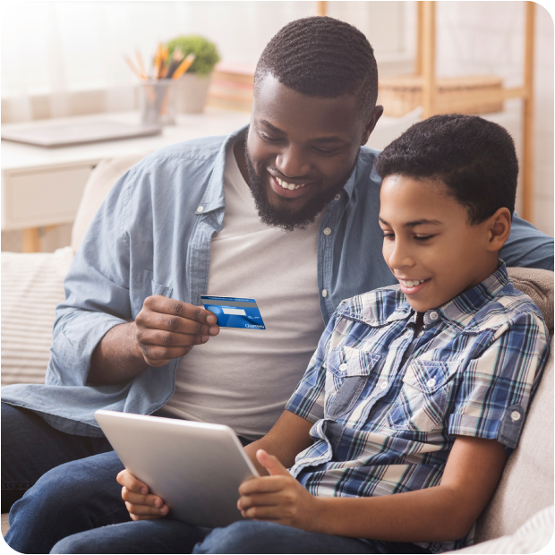 Father and son use tablet with debit card, highlighting Guardian CU youth checking and learning.