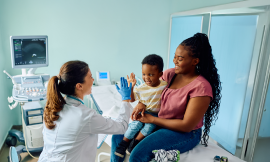 Mother holding a happy toddler high-fiving the doctor.