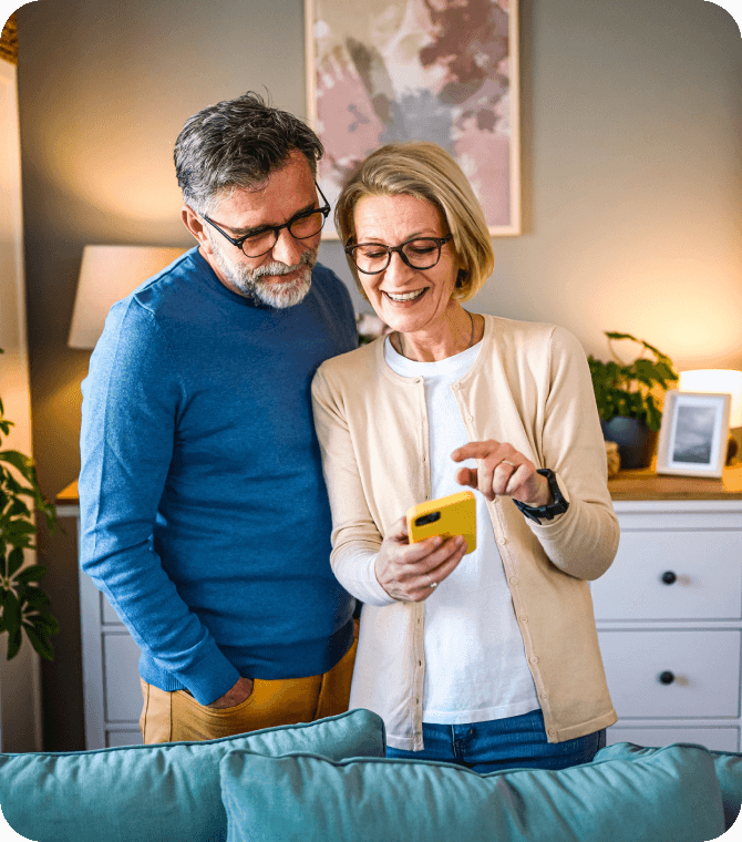 Smiling couple uses smartphone at home, representing confidence in Guardian CU online banking.