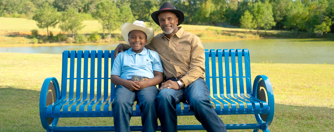 Grandfather and grandson smiling while sitting on a Guardian Credit Union bench at their farm.