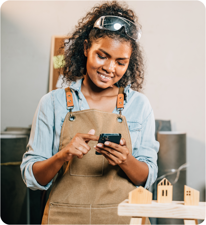 Smiling young woman at work holding a smartphone, appreciating the convenience of having her paycheck directly deposited into her Guardian Credit Union account.